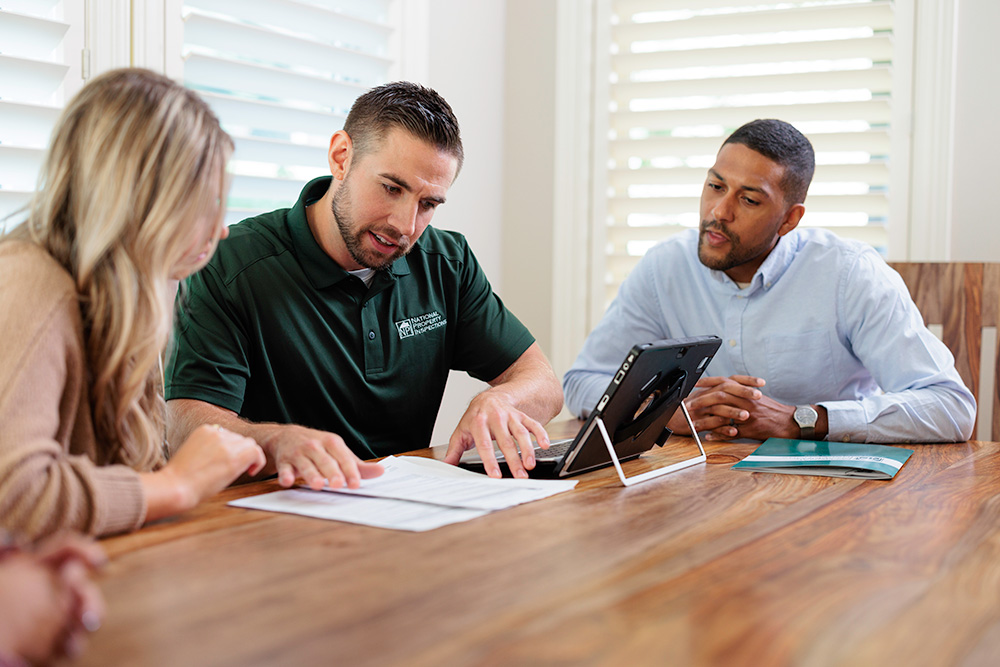 An NPI inspector discusses details in a home inspection report with his clients.