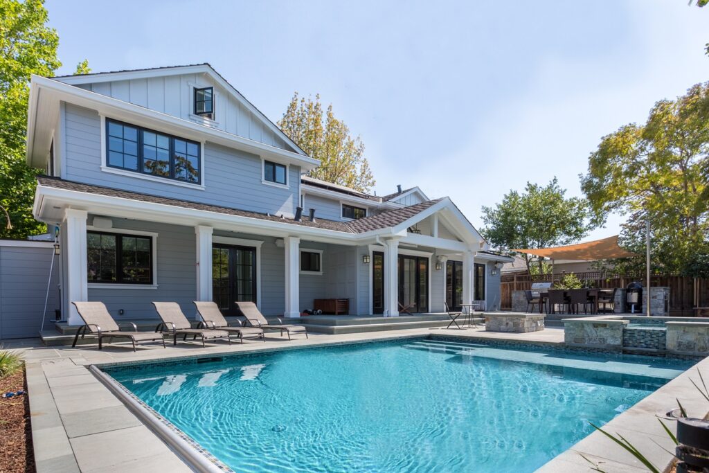 Outdoor view of home with in-ground pool and four lounge chairs on a sunny day.