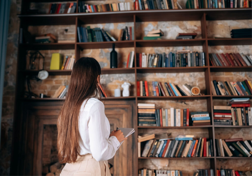 A young woman looks at a large bookshelf filled with books and decorations.