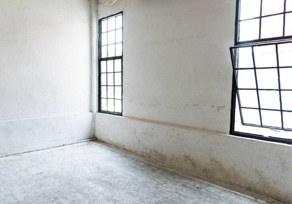 White industrial wall with two windows and stains near the floor.