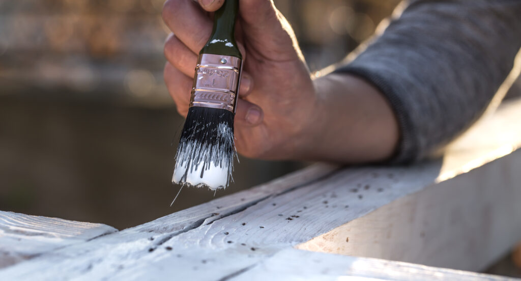 A paint brush applies paint to a wooden beam, symbolizing the use of lead paint.